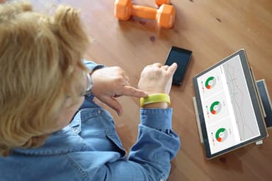 Older adult reviewing health tracking data on a tablet, wearing a fitness wristband, illustrating life sciences digital health technology