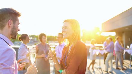 Smiling businesswoman drinking champagne while talking to colleague in rooftop success party.jpg